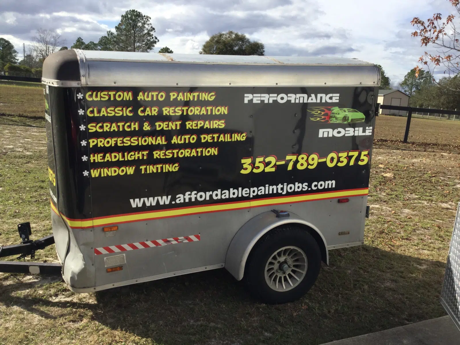 Branded work trailer parked on grass under cloudy sky — Performance Mobile Detail in Ocala
